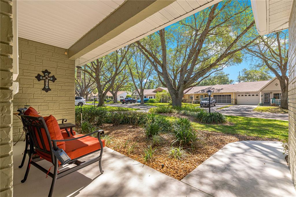A covered front porch with an orange chair overlooks a landscaped yard and neighborhood street — 9380 SW 84TH TERRACE UNIT C, OCALA, FL