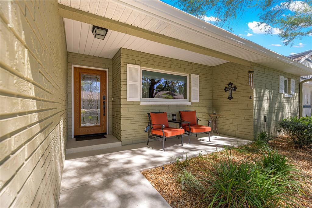 A covered front porch features olive green brick walls, two orange chairs, and a wooden door — 9380 SW 84TH TERRACE UNIT C, OCALA, FL