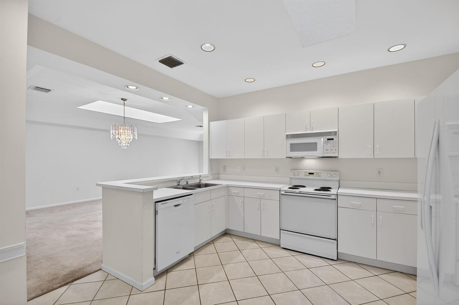 A white kitchen with tile flooring, white cabinets, and a breakfast bar overlooking a room — 12574 Crystal Pointe Drive # C, Boynton Beach FL 33437, BOYNTON BEACH, FL