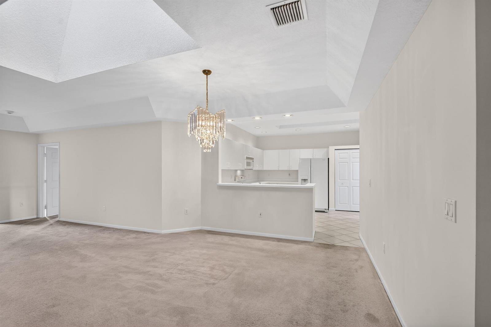 A carpeted living room with a crystal chandelier opens to a kitchen with white cabinets — 12574 Crystal Pointe Drive # C, Boynton Beach FL 33437, BOYNTON BEACH, FL