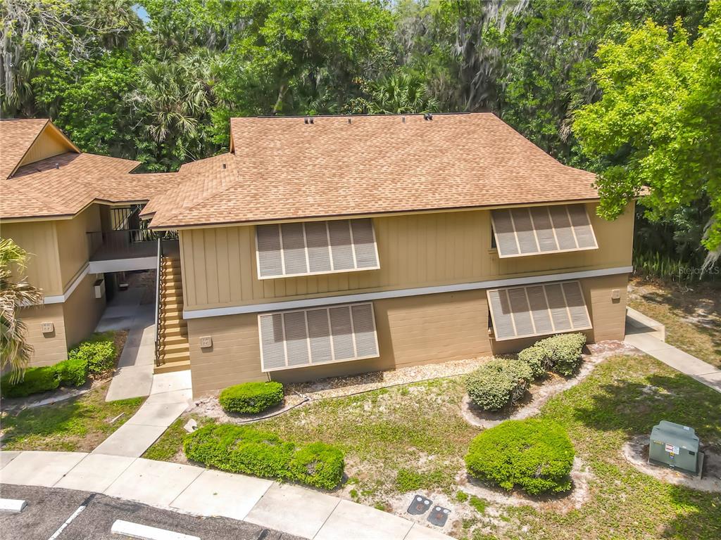 An exterior view of a two-story tan building with brown shutters and a shingled roof — 110 CYPRESS WOODS COURT UNIT 7D, DELTONA, FL