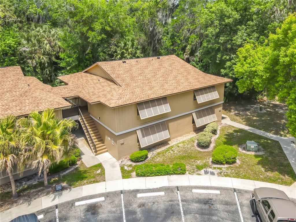 An elevated exterior view of a two-story tan apartment building with brown shingled roofs — 110 CYPRESS WOODS COURT UNIT 7D, DELTONA, FL
