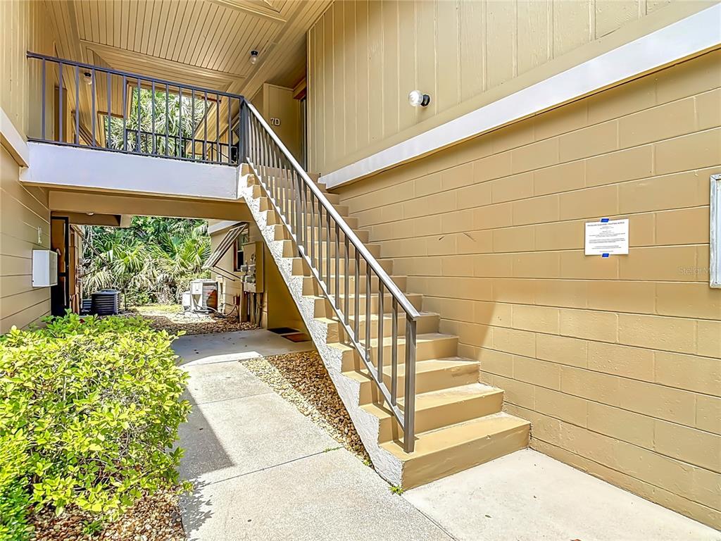 An exterior view of a tan building featuring a concrete staircase leading to an upper walkway — 110 CYPRESS WOODS COURT UNIT 7D, DELTONA, FL