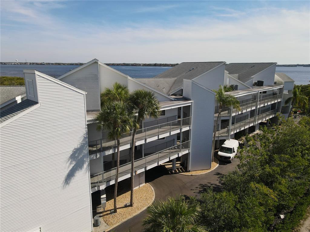 An aerial view shows a multi-story apartment building with exterior walkways and a waterfront location — 515 LEFFINGWELL AVENUE UNIT 116, ELLENTON, FL