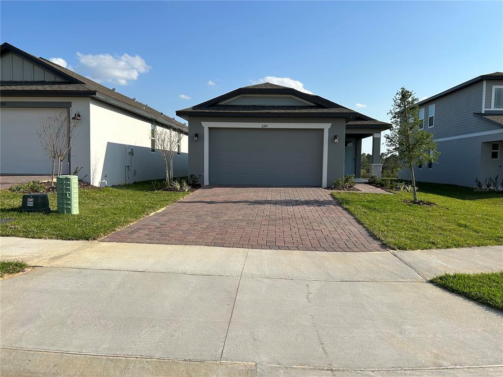 A single-story house with a gray garage, brick paver driveway, and a small front lawn — 2249 MYSTIC MAZE LANE, CLERMONT, FL
