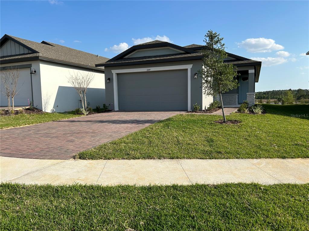 A single-story house with a gray garage, brick paver driveway, and a small front yard — 2249 MYSTIC MAZE LANE, CLERMONT, FL
