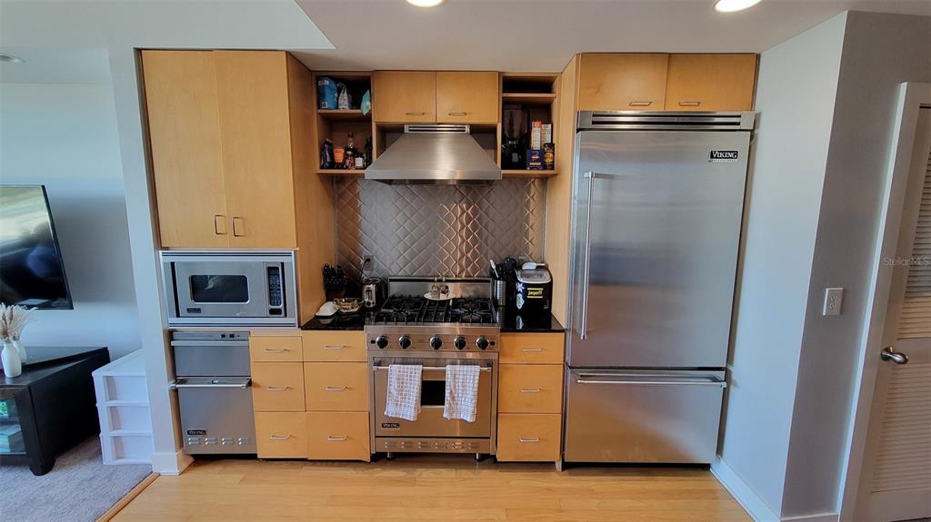 A kitchen features light wood cabinets, stainless steel appliances, and a diamond-patterned metal backsplash — 1120 E KENNEDY BOULEVARD UNIT 1217, TAMPA, FL