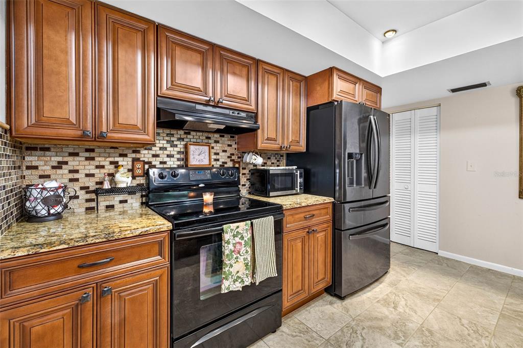 A kitchen features wood cabinets, granite countertops, a black stove, and a stainless steel refrigerator — 910 HILLSIDE DRIVE, LUTZ, FL