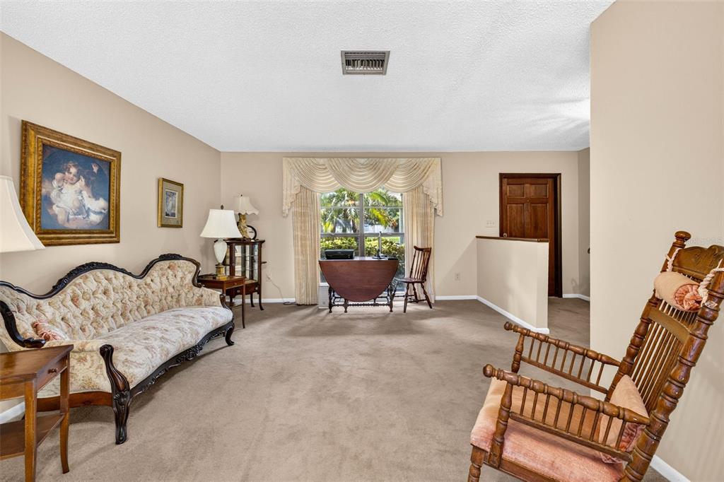 A carpeted living room features a vintage sofa, a wooden rocking chair, and a window — 910 HILLSIDE DRIVE, LUTZ, FL