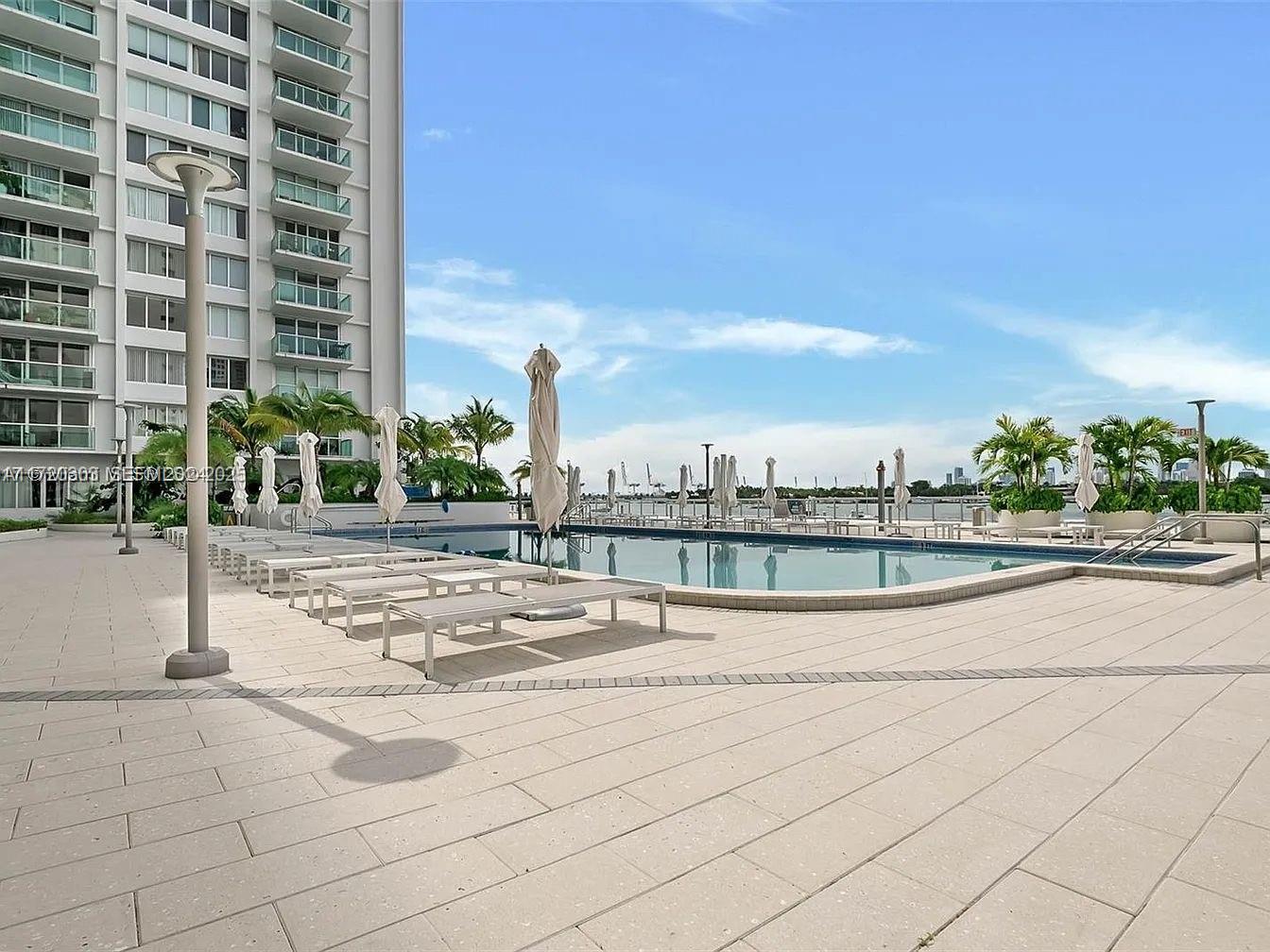 A swimming pool with lounge chairs sits on a paved deck beside a tall building — 1000 West Ave, Miami Beach FL 33139, MIAMI BEACH, FL