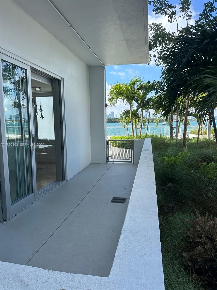 A concrete balcony overlooks a waterfront view with palm trees and a distant city skyline — 1000 West Ave, Miami Beach FL 33139, MIAMI BEACH, FL