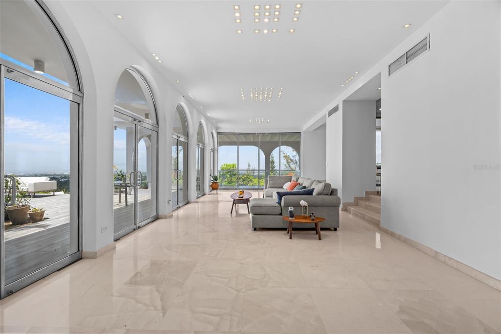 A spacious living room with light tile floors, arched glass doors, and a grey sectional sofa — 7 LA ROCA STREET BEVERLY HILLS, GUAYNABO, PR