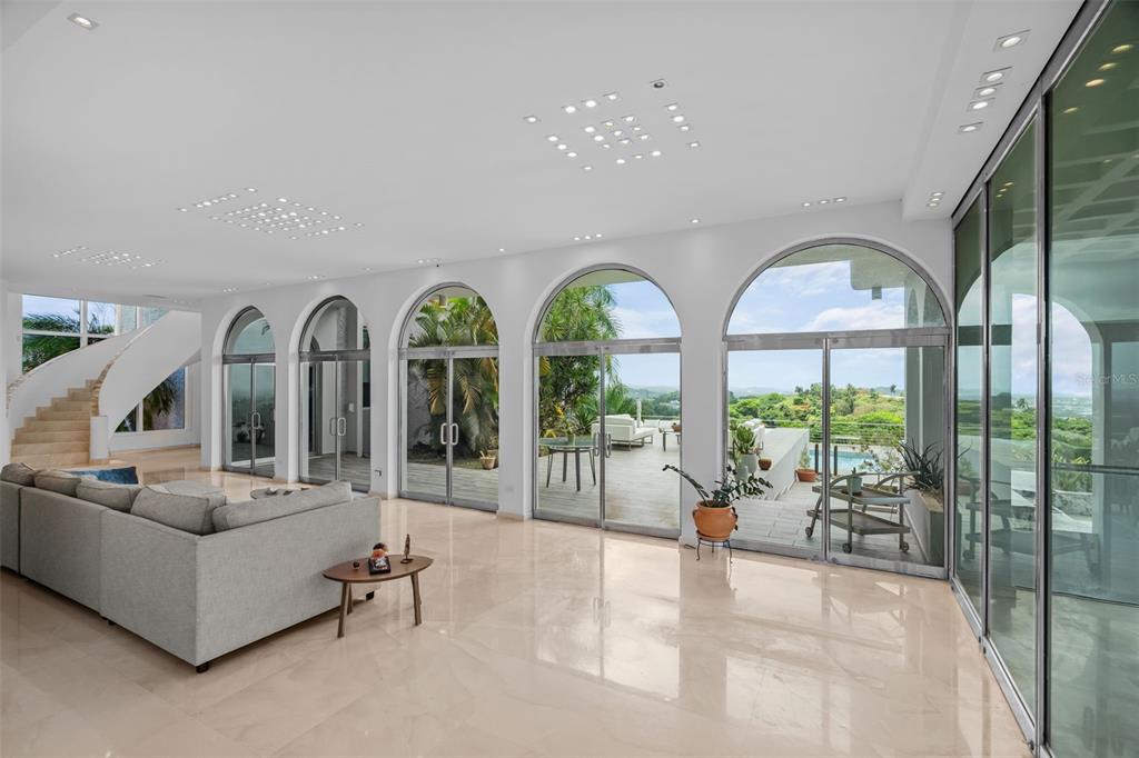 A spacious living room features arched glass doors, light tile floors, and a curved staircase — 7 LA ROCA STREET BEVERLY HILLS, GUAYNABO, PR