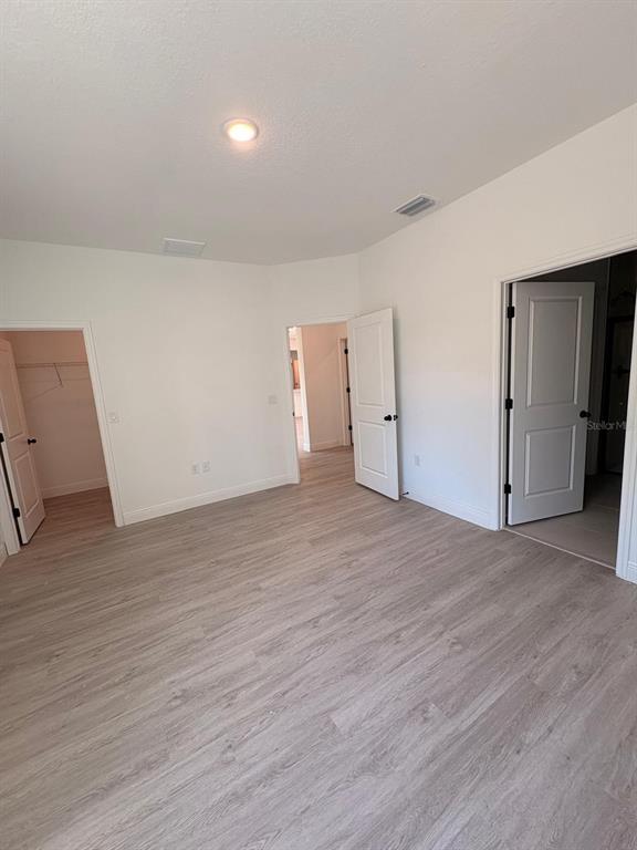 A bedroom with light wood-look flooring, white walls, and three open doorways — 7838 N SARAZEN DRIVE, CITRUS SPRINGS, FL