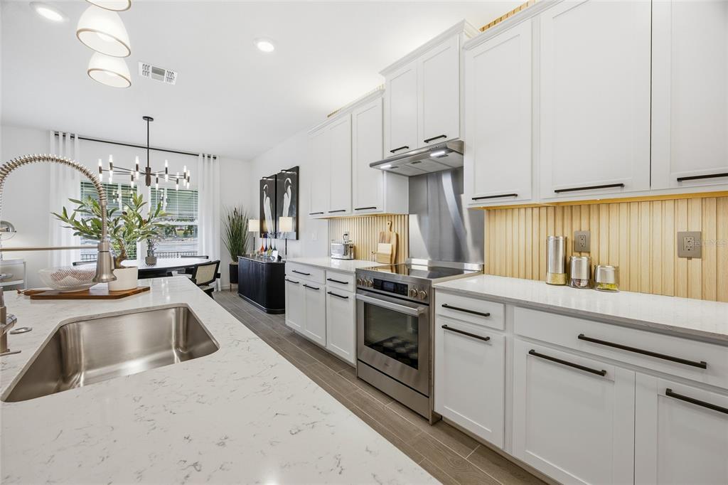 A modern kitchen features white cabinets, quartz countertops, a stainless steel range, and wood-slat backsplash — 8946 SW 67TH AVENUE, OCALA, FL