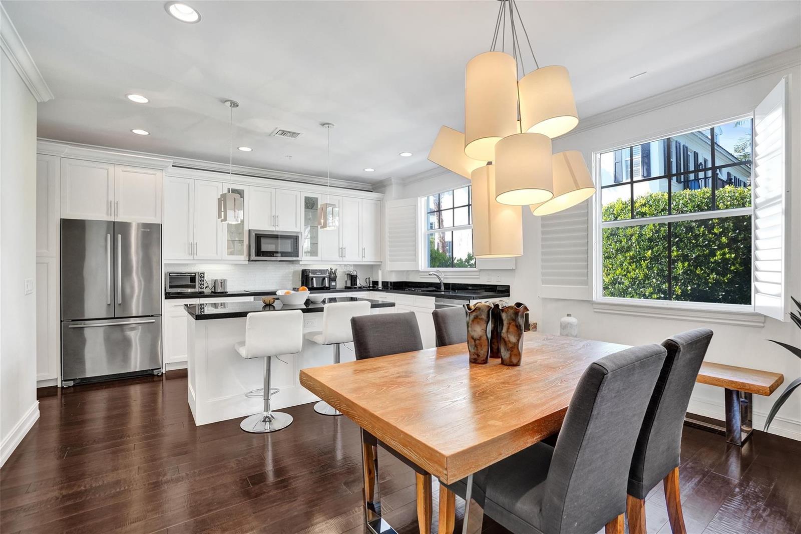 A kitchen and dining area features white cabinets, black countertops, and a wooden dining table — 381 E Cannery Row Circle, Delray Beach FL 33444, DELRAY BEACH, FL
