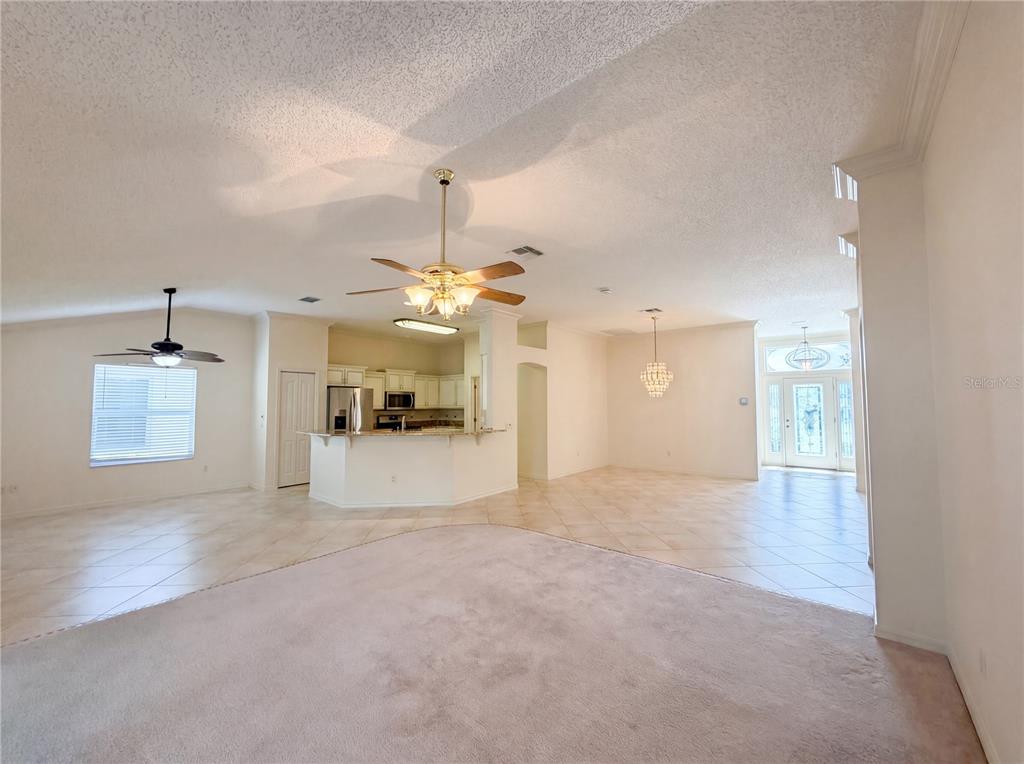A spacious open-concept living area features a carpeted foreground, tiled flooring, and a kitchen island — 1422 SEGOVIA PLACE, THE VILLAGES, FL