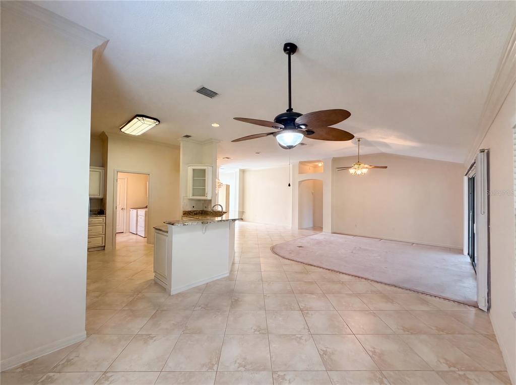 An open-concept living area features tile flooring, a kitchen island, and a carpeted living space — 1422 SEGOVIA PLACE, THE VILLAGES, FL