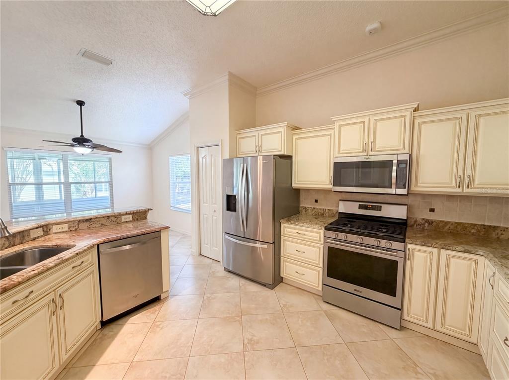 A kitchen with cream-colored cabinets, stainless steel appliances, granite countertops, and tile flooring — 1422 SEGOVIA PLACE, THE VILLAGES, FL