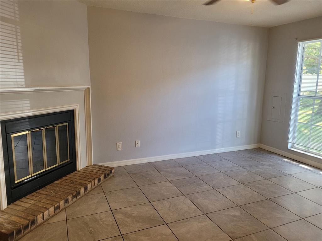 A living room features a brick-hearth fireplace, tile flooring, and a window with blinds — 11301 GRANDVILLE DRIVE, TEMPLE TERRACE, FL