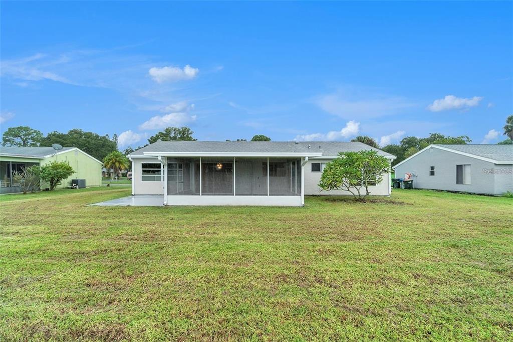 The rear exterior of a single-story house features a screened-in porch and a grassy yard — 5052 TREKELL STREET, NORTH PORT, FL