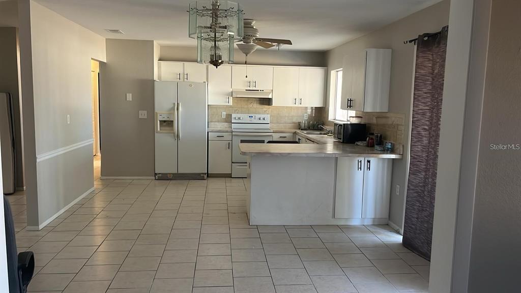 A kitchen features white cabinets, white appliances, a peninsula, and light-colored tile flooring — 5052 TREKELL STREET, NORTH PORT, FL