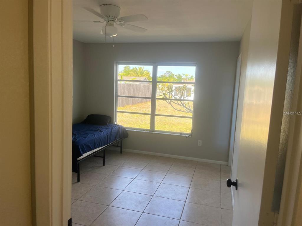 A bedroom with light-colored tile flooring, a ceiling fan, and a window overlooking a yard — 5052 TREKELL STREET, NORTH PORT, FL