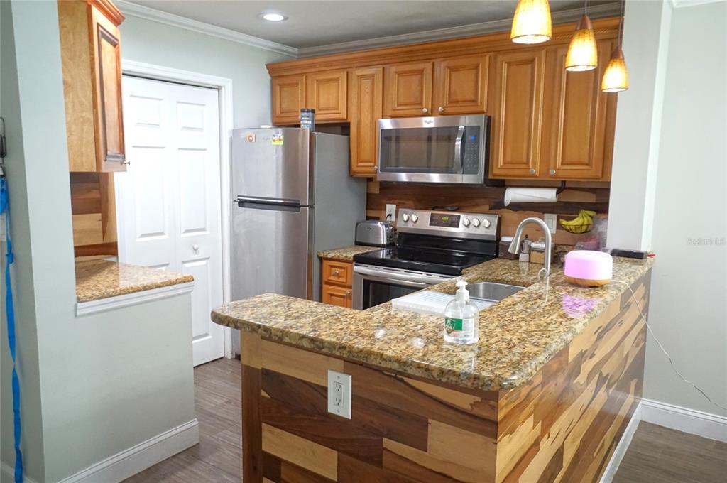 A kitchen features wood-paneled cabinetry, granite countertops, stainless steel appliances, and a wood-accented breakfast bar — 10122 WINSFORD OAK BOULEVARD UNIT 409, TAMPA, FL
