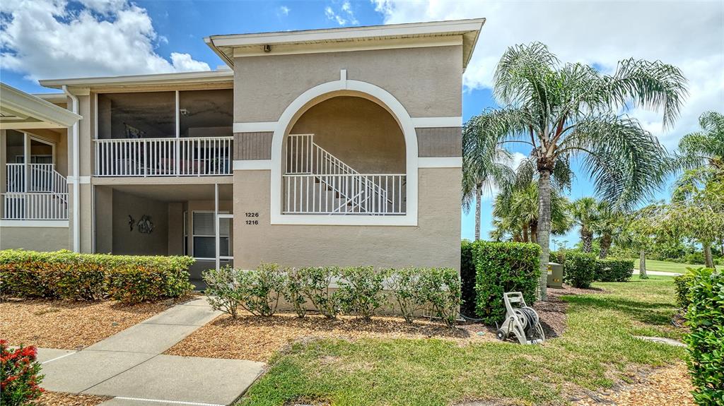 A two-story tan stucco building features a screened balcony, arched entryway, and landscaped grounds — 9641 CASTLE POINT DRIVE UNIT 1226, SARASOTA, FL