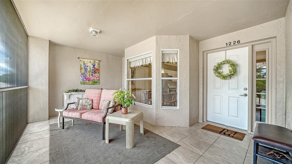 A covered patio features tiled flooring, a plaid loveseat, and a white front door — 9641 CASTLE POINT DRIVE UNIT 1226, SARASOTA, FL