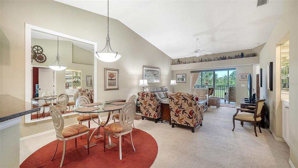 A dining area with a glass table and a living room with vaulted ceilings — 9641 CASTLE POINT DRIVE UNIT 1226, SARASOTA, FL