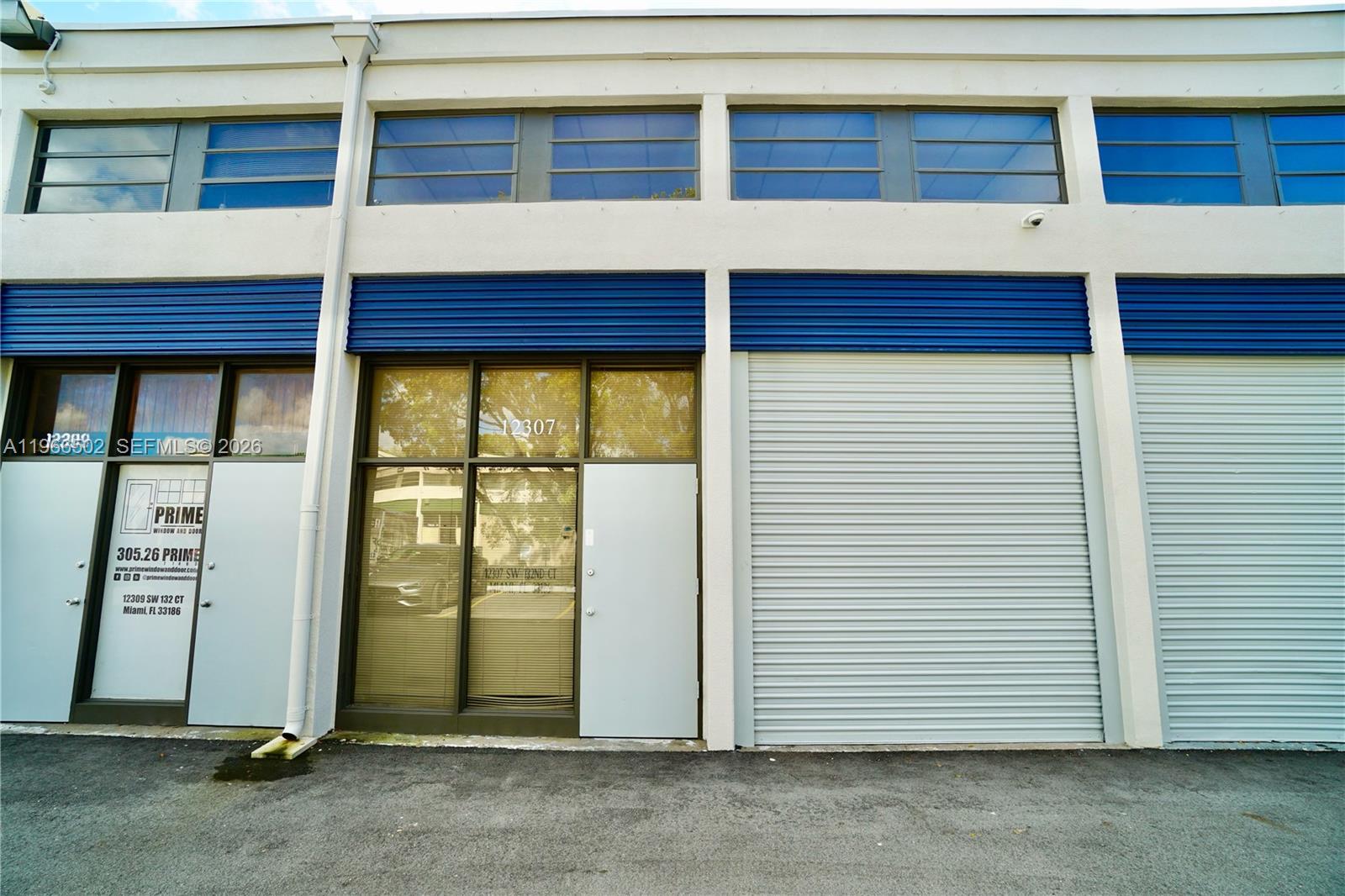 A commercial building exterior features a glass entrance door, a roll-up metal door, and windows — 12307 SW 132nd Ct # 4, Miami FL 33186, MIAMI, FL