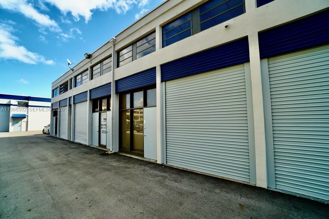 An exterior view of a commercial building with multiple roll-up doors and glass entryways — 12307 SW 132nd Ct # 4, Miami FL 33186, MIAMI, FL