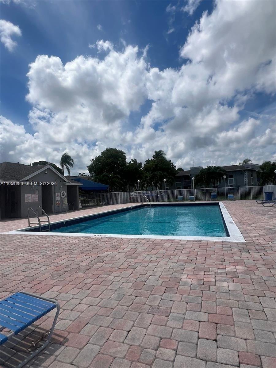 A rectangular swimming pool is surrounded by a brick paver deck and a white fence — 455 NE 210th Cir Ter # 18, Miami FL 33179, MIAMI, FL