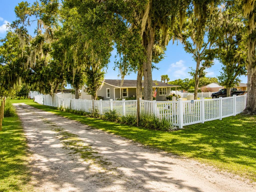 A single-story house with a white fence and large trees sits beside a dirt driveway — 330 MOCCASIN HOLLOW ROAD, LITHIA, FL