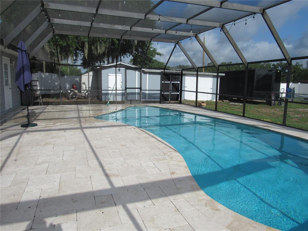 A screened-in patio features a swimming pool and light-colored stone pavers — 330 MOCCASIN HOLLOW ROAD, LITHIA, FL