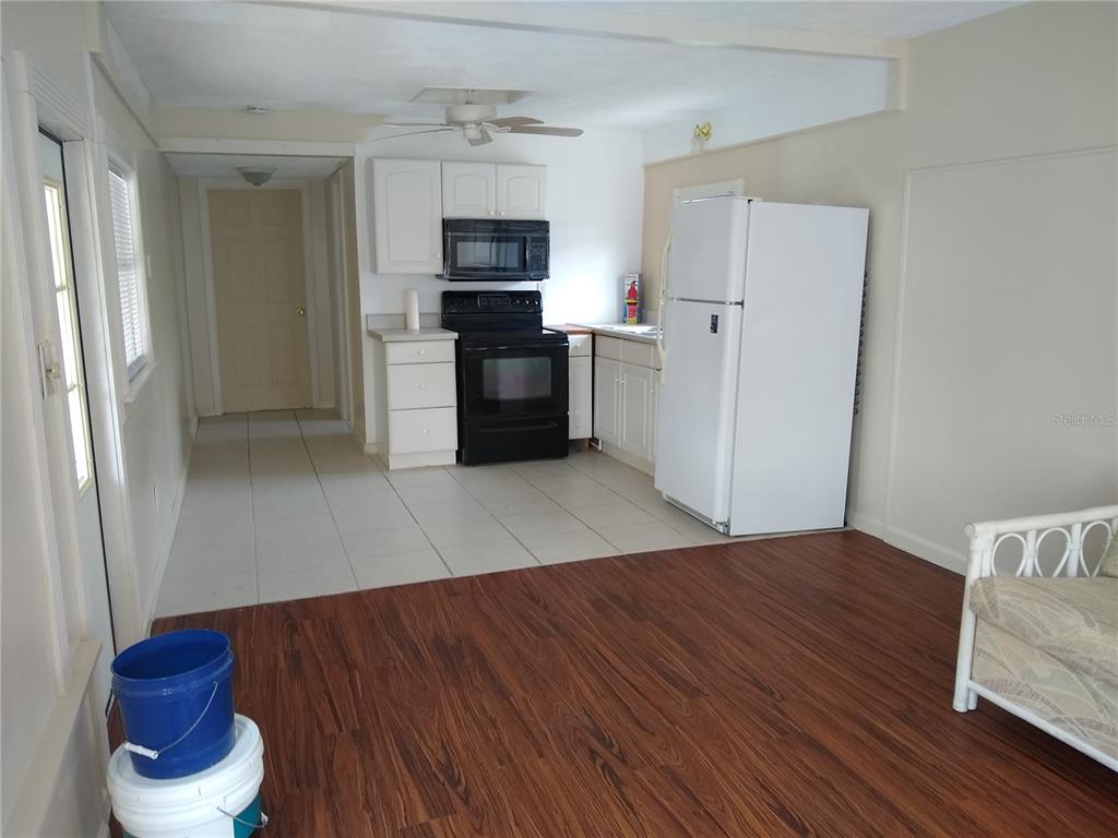 A kitchen with white cabinets, black appliances, and tile flooring transitions into a wood-floored living area — 205 52ND AVENUE DRIVE W, BRADENTON, FL