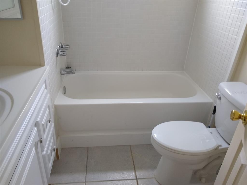 A bathroom features a white vanity, a tiled bathtub shower combo, and a white toilet — 205 52ND AVENUE DRIVE W, BRADENTON, FL