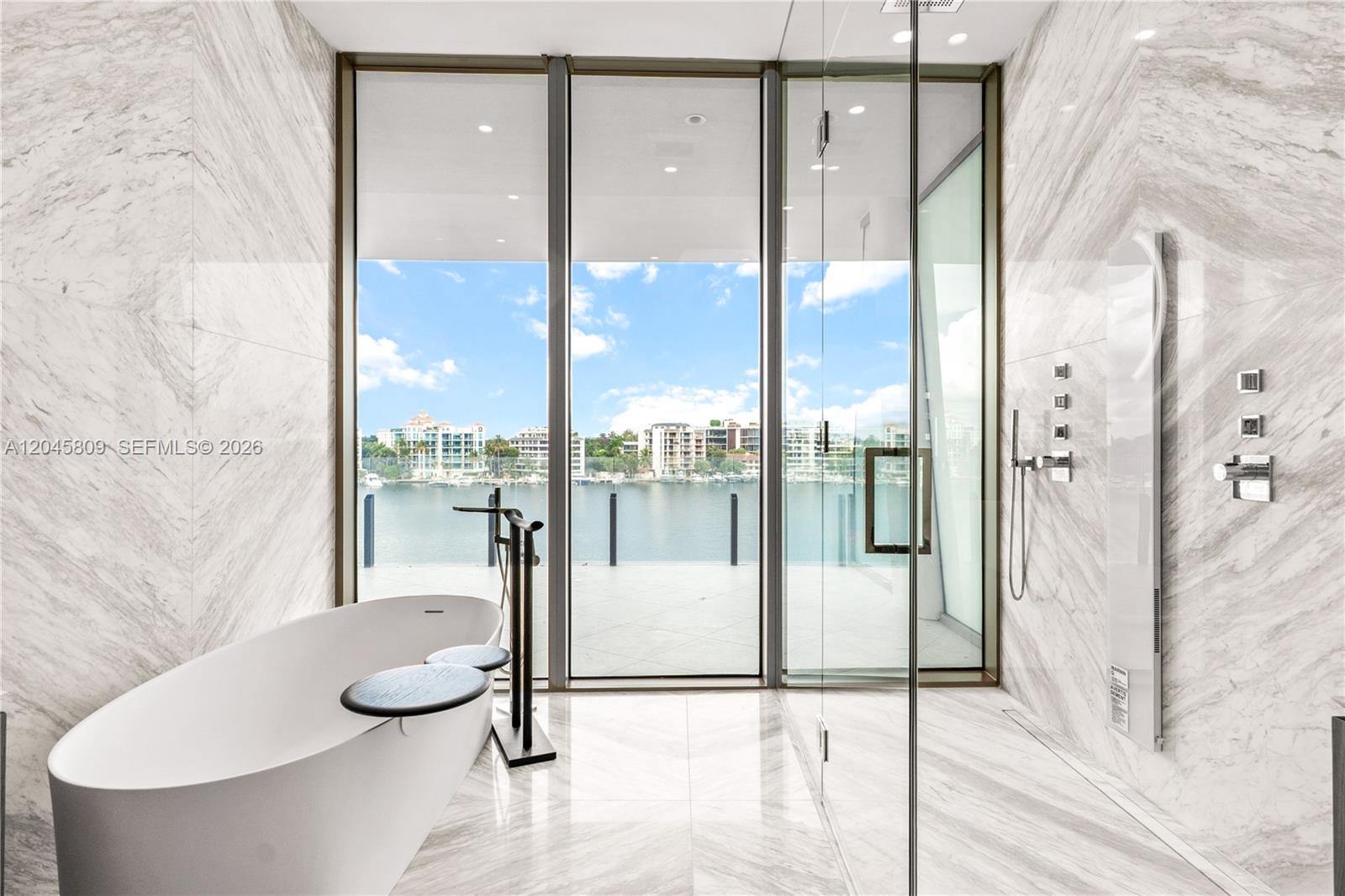 A modern bathroom features a freestanding tub, glass-enclosed shower, and floor-to-ceiling windows overlooking water — 5 Grove Isle # L405, Miami FL 33133, MIAMI, FL