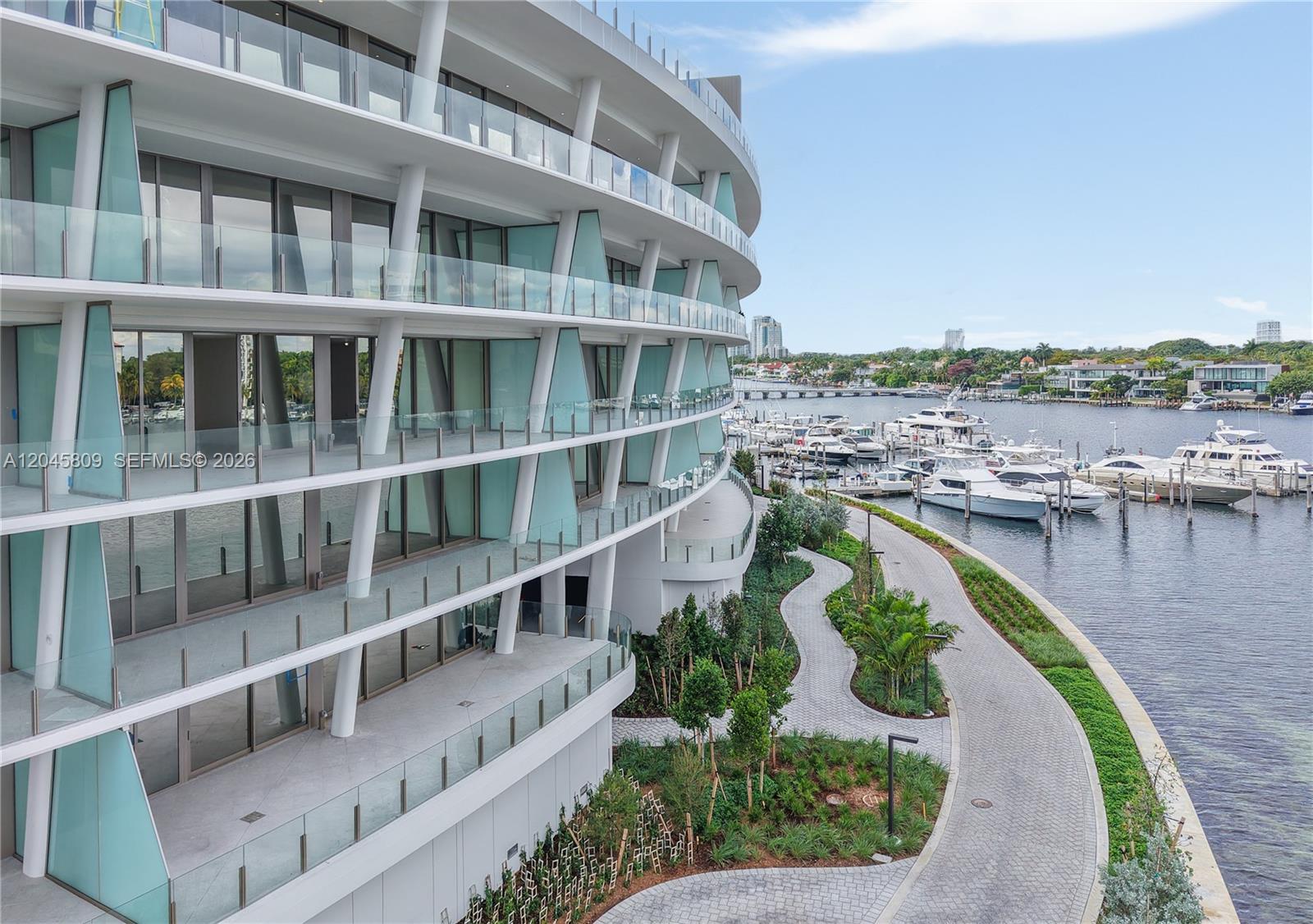 An exterior view of a modern curved building with glass balconies overlooking a boat marina — 5 Grove Isle # L405, Miami FL 33133, MIAMI, FL