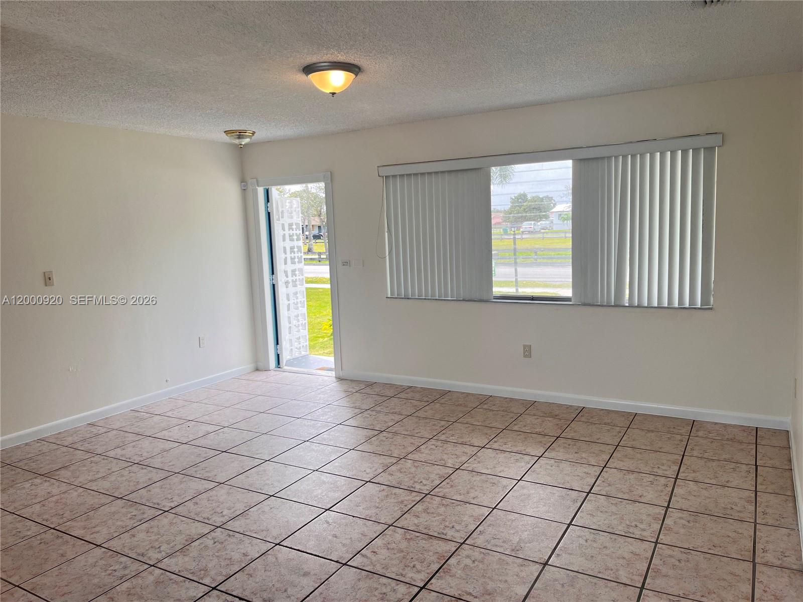 An empty room features beige tile flooring, white walls, a ceiling light, and vertical blinds — 20341 SW 117th Ave, Miami FL 33177, MIAMI, FL