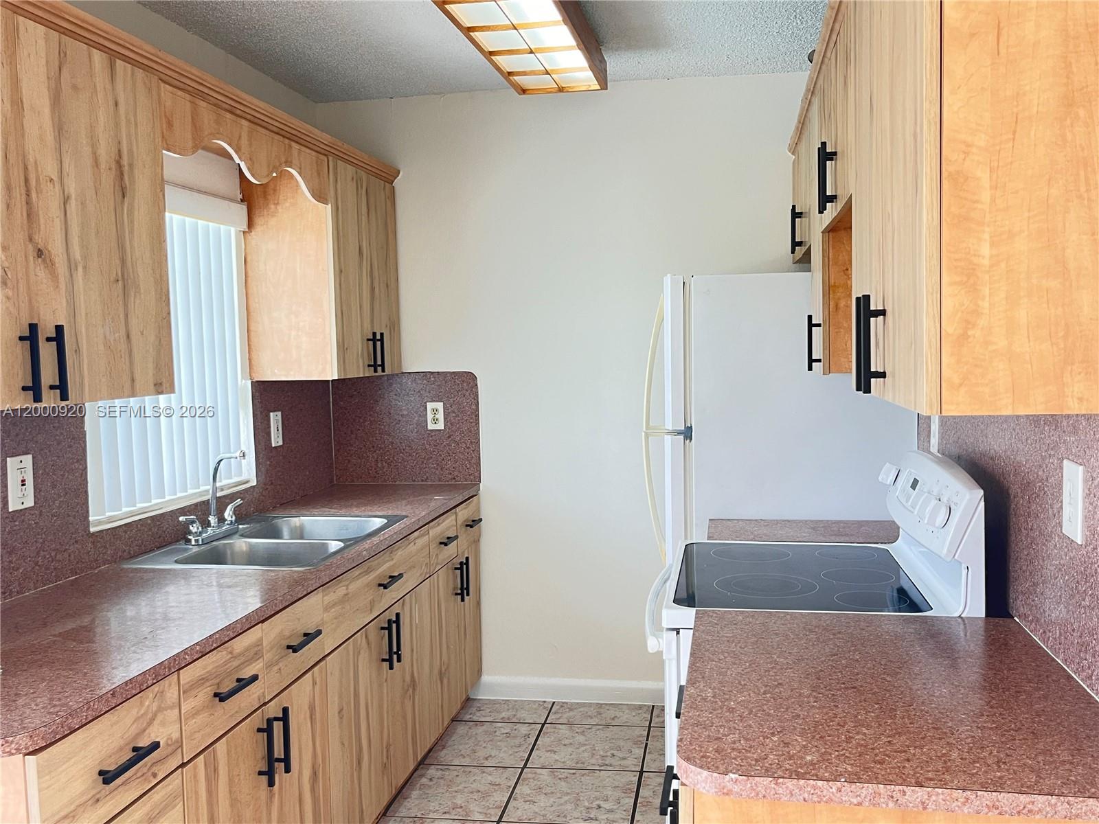 A kitchen features wood-grain cabinets, dark countertops, a white refrigerator, and a glass-top stove — 20341 SW 117th Ave, Miami FL 33177, MIAMI, FL
