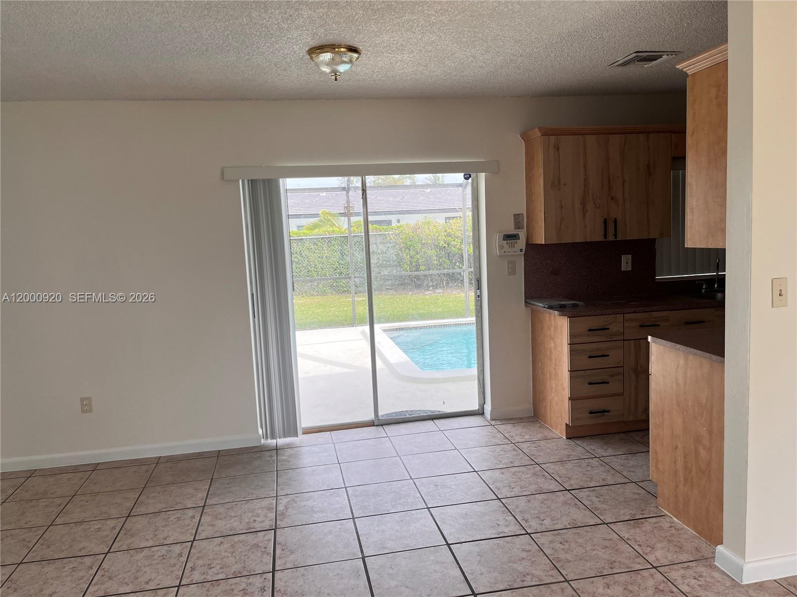 A kitchen and dining area with tile floors, wooden cabinets, and a sliding door to a pool — 20341 SW 117th Ave, Miami FL 33177, MIAMI, FL