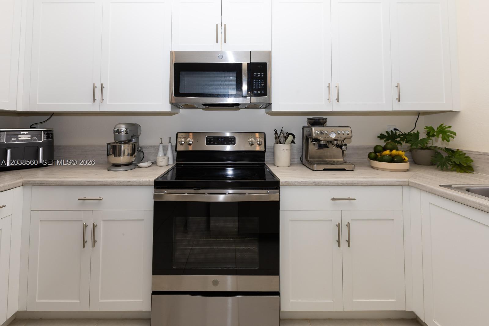 A kitchen features white cabinets, stainless steel appliances, and light-colored countertops — 3420 W 111th Pl, Hialeah FL 33018, HIALEAH, FL