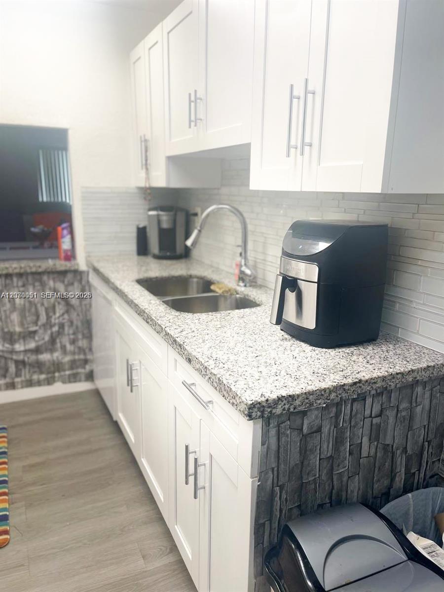 A kitchen features white cabinets, granite countertops, a stainless steel sink, and stone-tiled walls — 177 Lakeview Dr # 104, Weston FL 33326, WESTON, FL