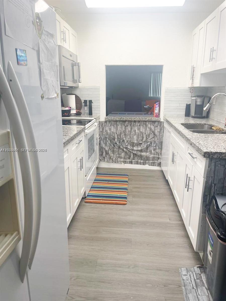 A galley-style kitchen features white cabinets, granite countertops, and light wood-look flooring — 177 Lakeview Dr # 104, Weston FL 33326, WESTON, FL