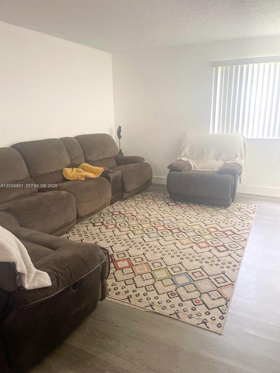 A living room features brown reclining furniture, a patterned area rug, and a window with blinds — 177 Lakeview Dr # 104, Weston FL 33326, WESTON, FL