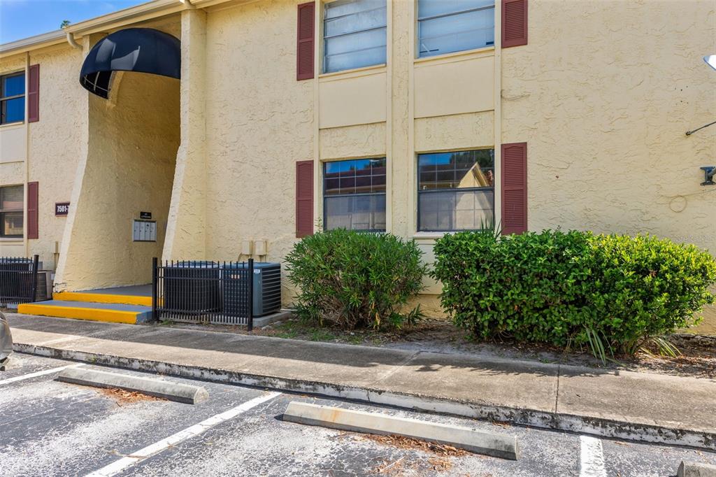 Exterior view of a two-story apartment building with yellow stucco walls and a parking lot — 7501 DOLONITA DRIVE UNIT 7501, TAMPA, FL