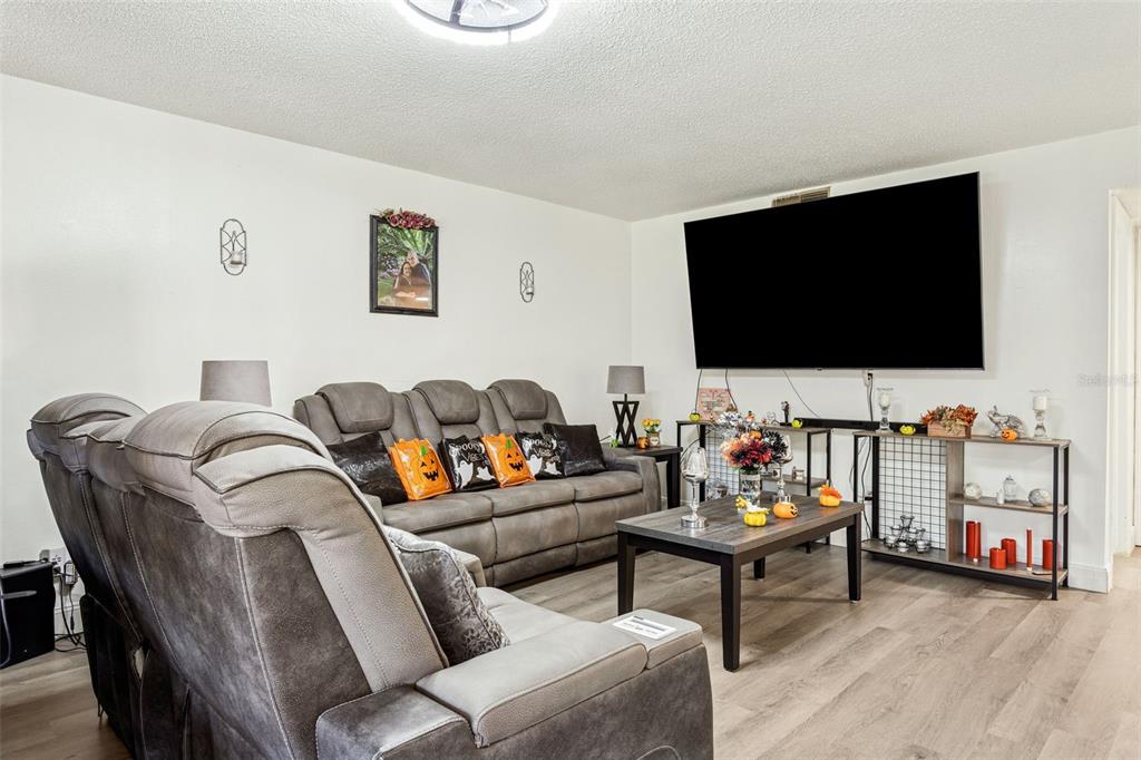A living room features gray reclining sofas, a coffee table, and a large wall-mounted television — 7501 DOLONITA DRIVE UNIT 7501, TAMPA, FL