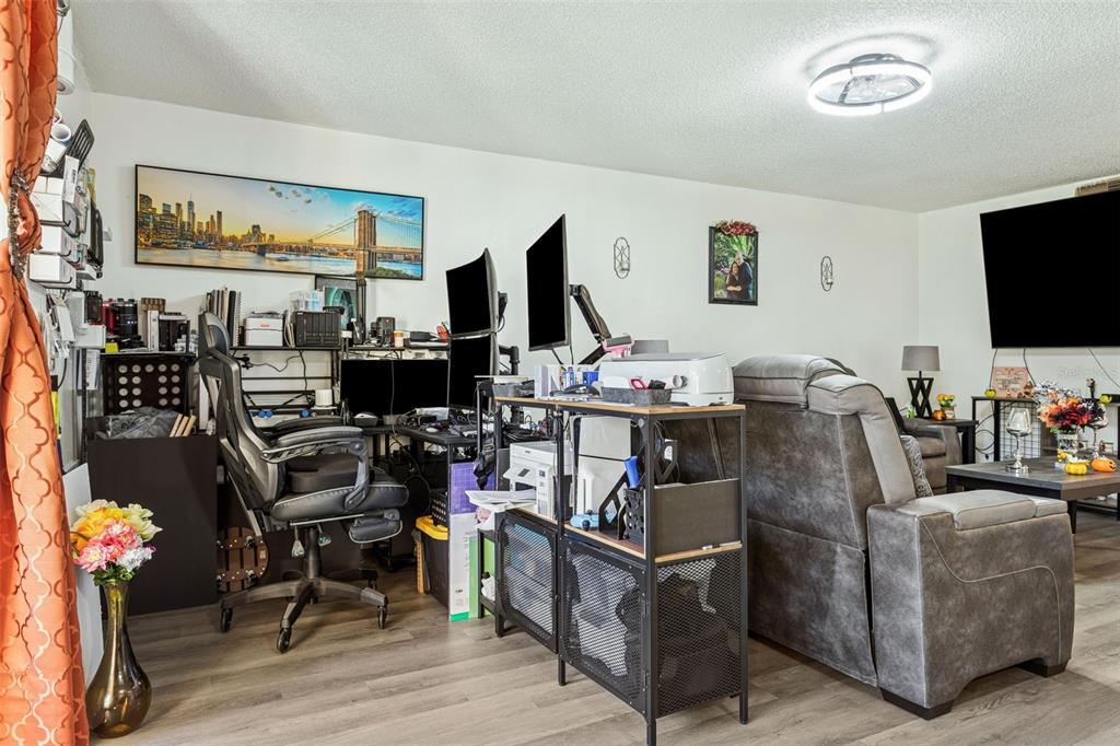 A living room features a home office setup, a gray recliner, and a wall-mounted television — 7501 DOLONITA DRIVE UNIT 7501, TAMPA, FL